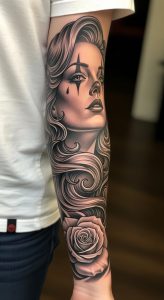 Realistic black and grey forearm sleeve tattoo portrait with flowing hair, teardrop, and rose